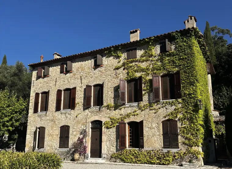 Une bastide en pierre couverte de vigne vierge, aux volets de bois